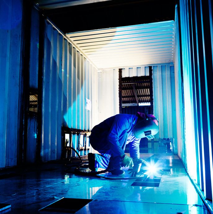 Welder working to modify container in steel fabrication plant